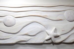 9" X 22" X 1.5", SAND SCRAWL is a wood sculpture that celebrates The Master Artisan's ever-changing sand-sculpture scrawled into the beaches of the world. The simple
yet gorgeous textures and forms carved into this endless sand-canvas are some of the most wondrous sights on the planet. Of course, The Master Artisan uses water
and wind to shape and smooth the infinite grains in a continual dance of creative beauty. Even the occasional starfish and sand dollar play into His artwork, interacting
with the forms in a sublime act of beauty-making. As a merely human artist, I'm joyfully humbled by the profound brilliance of The Master Artisan's technique and results.
To honor Him, I choose wood with a grain pattern that mirrors the undulating contours of sculpted sand. Then, I use various carving and sanding techniques to shape the
wood, taking care to account for its interplay with the sea creatures that I've placed in the composition. What He does in a moment takes me much, much longer. Still, I
hope that you appreciate the result and celebrate the original that inspired it.Radiant Pine forested from Sustainable-Sources